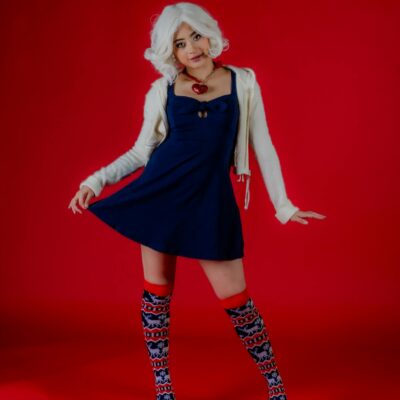 A fashionable woman poses in a blue dress with patterned socks on a red backdrop. Cosplay-inspired look.