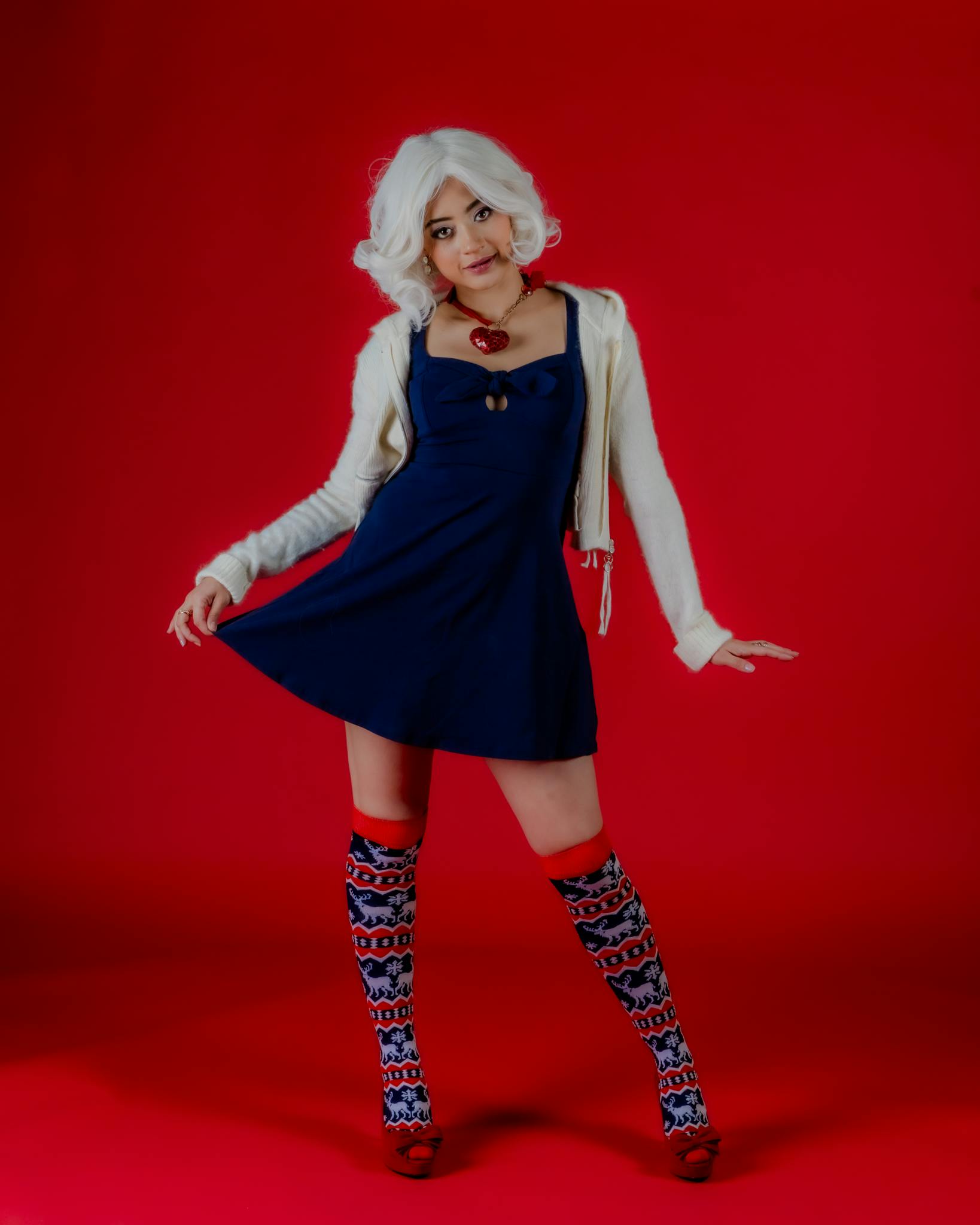 A fashionable woman poses in a blue dress with patterned socks on a red backdrop. Cosplay-inspired look.