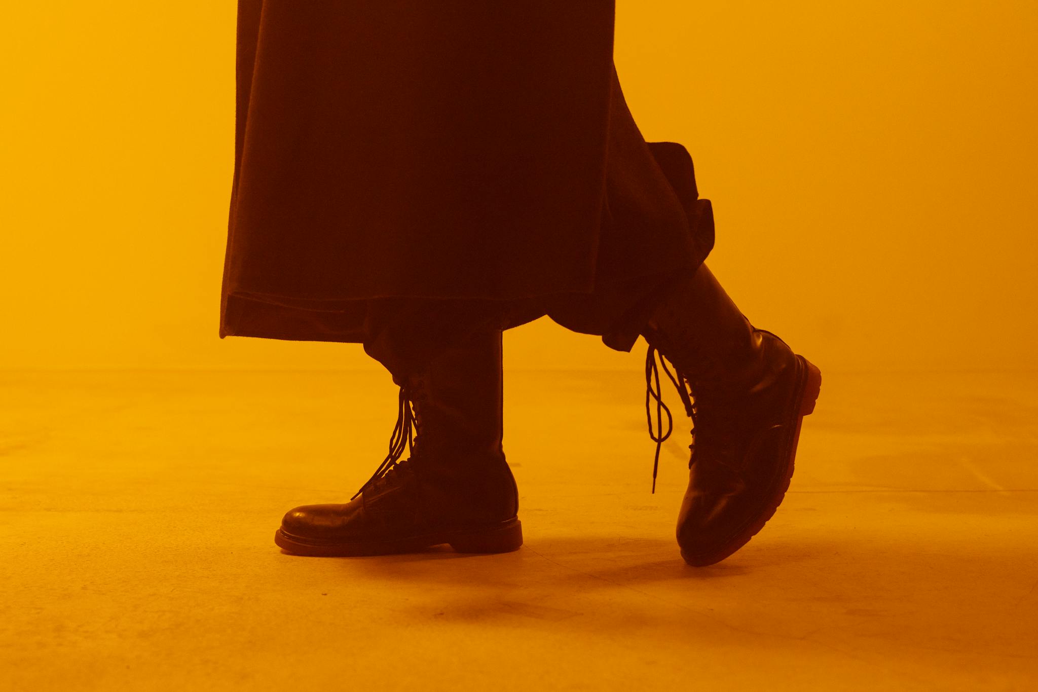 Close-up of black boots with laces in a dramatic, warm-toned studio setting.