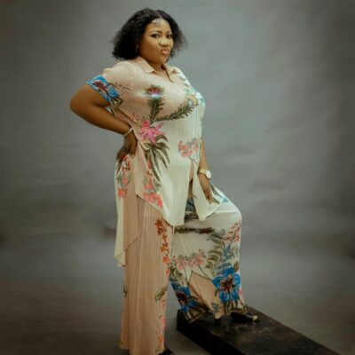 Confident woman in floral attire poses for a fashion shoot against a studio backdrop.