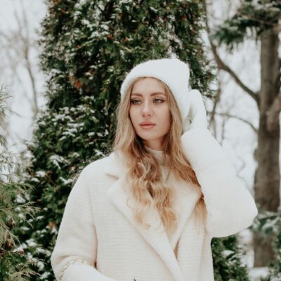 Stylish woman in winter attire posing amidst snow-covered trees.