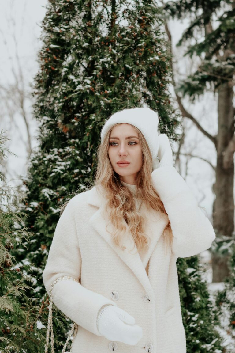 Stylish woman in winter attire posing amidst snow-covered trees.