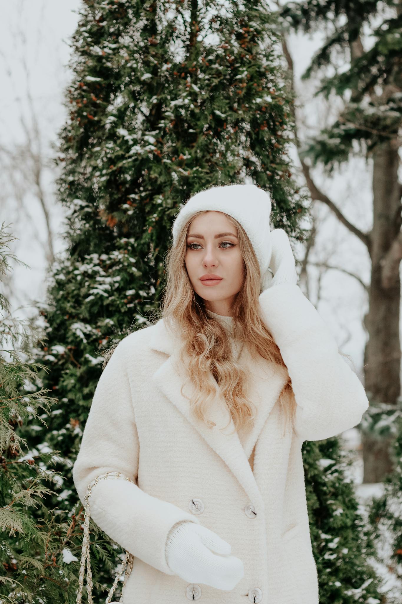 Stylish woman in winter attire posing amidst snow-covered trees.